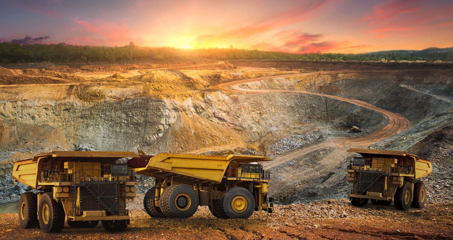 Open-pit mining operations with heavy haul trucks at sunset